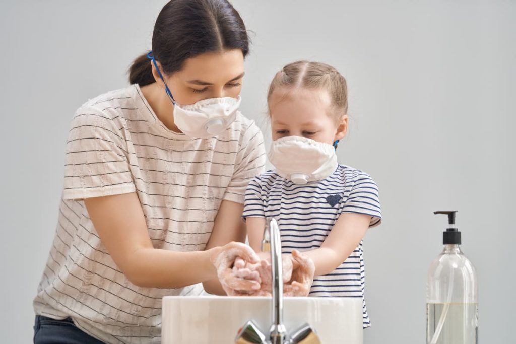 mamma e figlia con mascherine lavano le mani